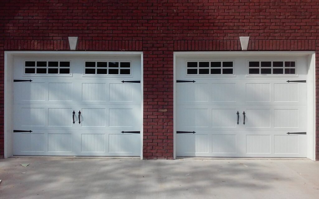Two newly installed white garage doors with windows and decorative hardware on a brick house by Ken's Overhead Door, Clarksville, TN.