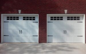 Two newly installed white garage doors with windows and decorative hardware on a brick house by Ken's Overhead Door, Clarksville, TN.