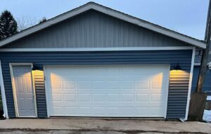 A newly installed white residential garage door on a blue-sided house by Tri County Overhead Door Service Inc in New London, WI.