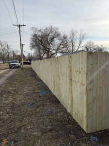 A newly installed wood privacy fence by Heath's Outdoor Services LLC in Champaign, IL, along a dirt path.