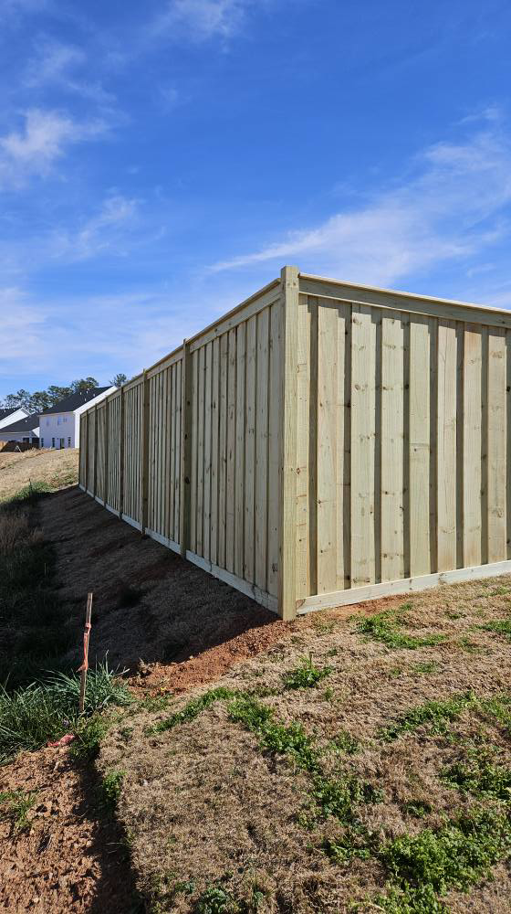 A newly installed light-colored wood privacy fence on a sloped property by The Fence Guy One in Greenville, SC.