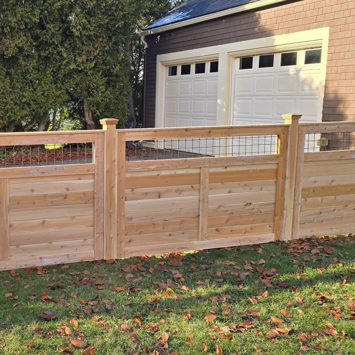 A newly installed wood and wire mesh fence in front of a garage by Midcoast Fence in Northport, ME.