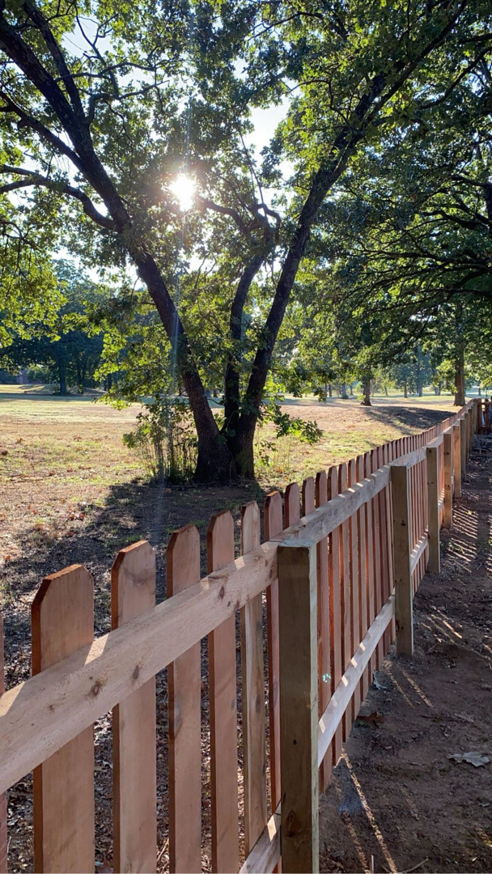 A long line of newly installed wooden picket fence by Fianna Fencing Company in Fort Smith, AR, bordering a field.