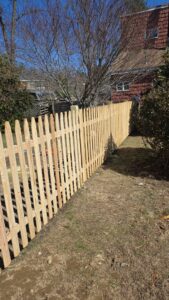A newly installed wooden picket fence extending along a property line by Matul Fence Inc in Lynn, MA