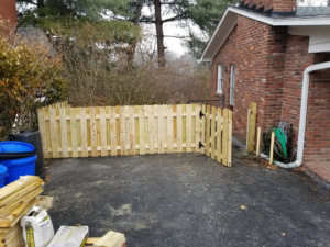 A newly installed wooden picket fence with a gate next to a brick house by Valkyrie construction, LLC in Granville, OH.