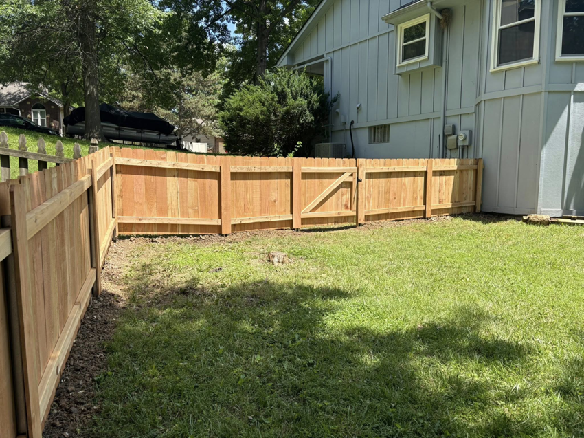 A newly installed wooden privacy fence with a gate in a residential backyard by Fry's Fence LLC in Grain Valley, MO.