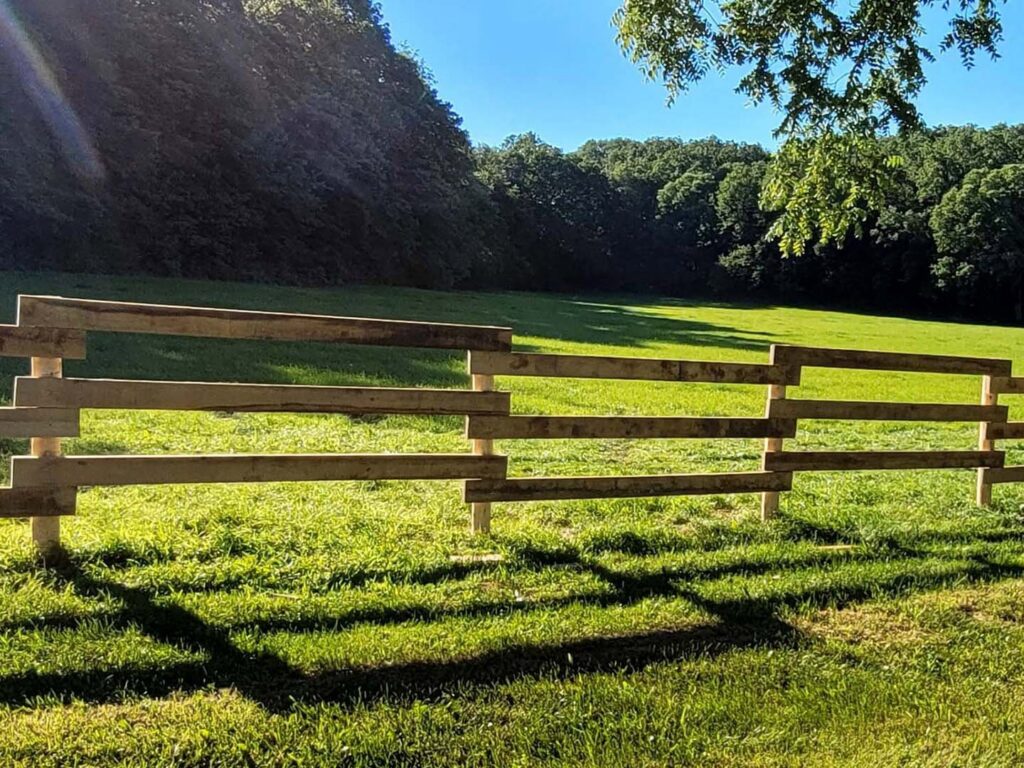 A newly installed wooden rail fence standing in a green grassy field, built by H&S Fencing & Supply in Linden, WI.