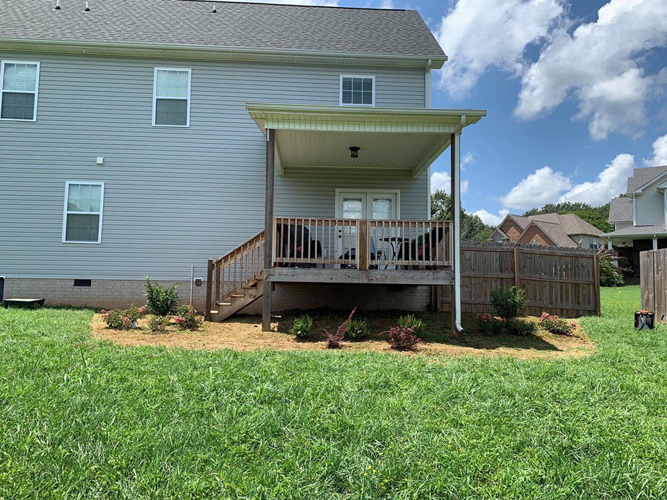 Newly planted and mulched backyard flower beds around a deck by Cutting Edge Lawn Services in Islip, NY
