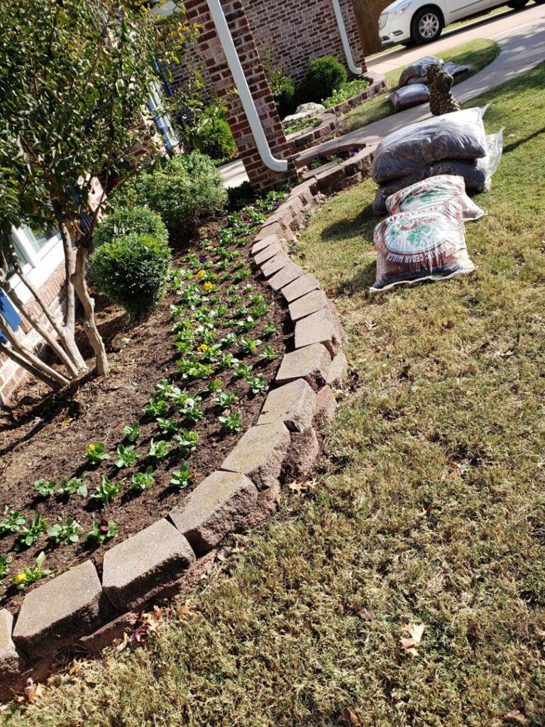 A newly planted flower bed with a stone border and bags of mulch by GAMAS Lawn Care Services in Tulsa, OK.