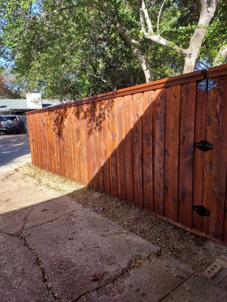 A newly stained wooden privacy fence with a gate featuring black hinges, installed by True Ways Services LLC in Mesquite, TX.