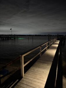 A long wooden dock illuminated by pathway lights at night, showcasing electrical lighting services by New York Electrical Design in Freeport, NY