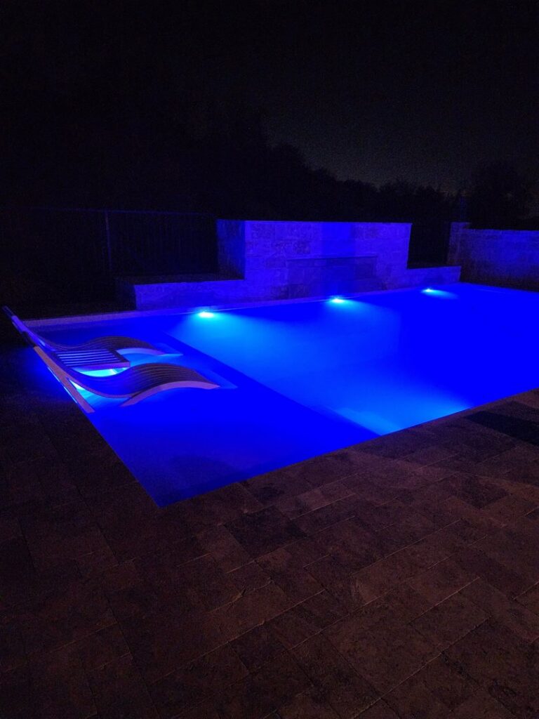 A beautifully lit pool at night with vibrant blue LED lights and an in-pool lounge chair by EZ POOL Solutions in Tucson, AZ
