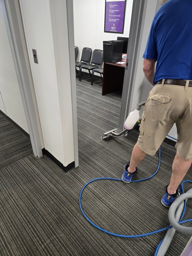 A professional cleaning a striped office carpet in a hallway by On The Spot Carpet and Upholstery Cleaning in Warren, MI.