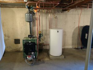 An oil burner service installation showing a green boiler and a white water heater by Nate's Oil Burner Service in New Bedford, MA