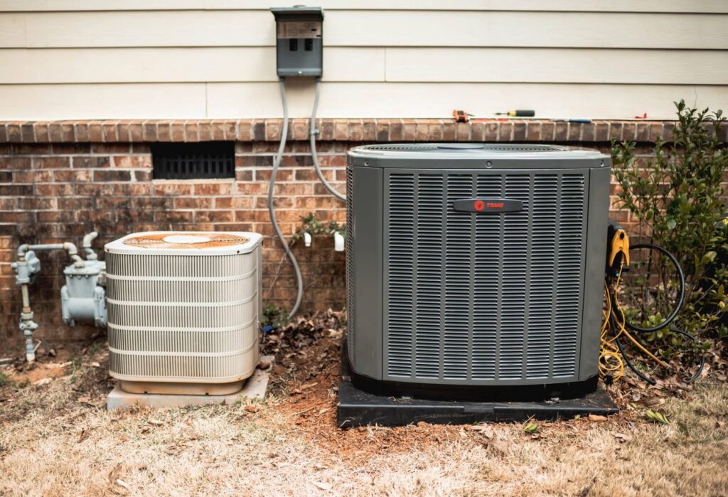 An old and a new Trane outdoor AC condenser unit side-by-side, indicating replacement by Wingman Heating + Cooling in Auburn, AL.