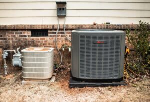 An old and a new Trane outdoor AC condenser unit side-by-side, indicating replacement by Wingman Heating + Cooling in Auburn, AL.