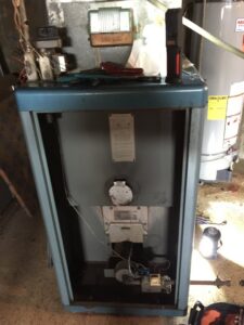 An old boiler or furnace with its front panel removed, showing internal components during a repair service by Around The Town Heating and Cooling in Chicago, IL.