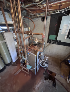 An old boiler heating system with extensive copper piping and pumps, undergoing repair or maintenance by HomeStyle Heating and Air LLC in Barrington, NH.