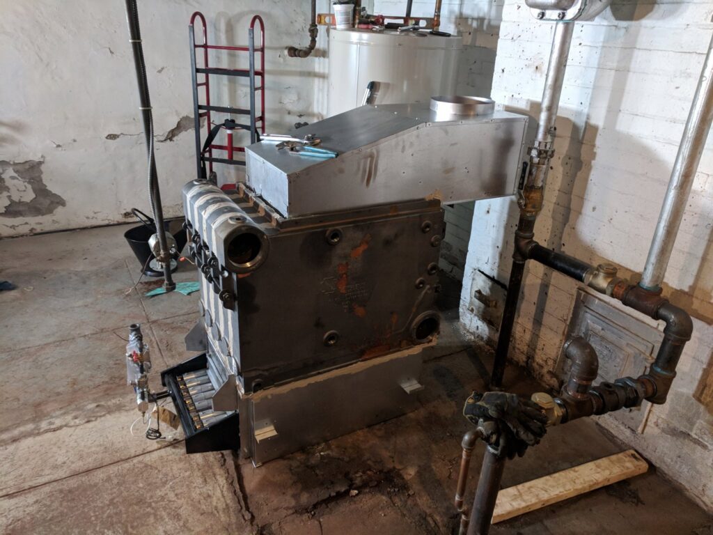 An old boiler unit being replaced or serviced by Huether Heating & Cooling Inc in a Rochester, NY basement.