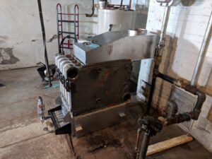 An old boiler unit being replaced or serviced by Huether Heating & Cooling Inc in a Rochester, NY basement.