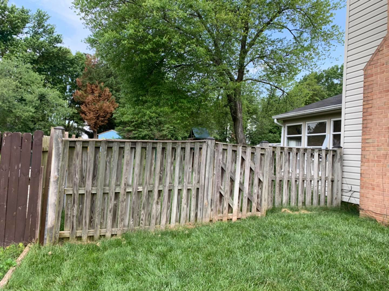 An old, damaged wooden privacy fence with a broken gate, showing a before-repair scene by Arias Fence & Repair in Manassas, VA.