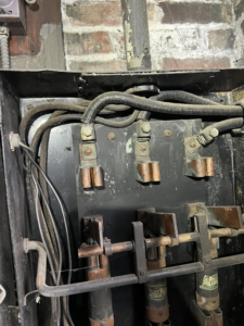 A close-up of an old electrical fuse panel with large wires and terminals, serviced by KNK Electric in Pittsburgh, PA.