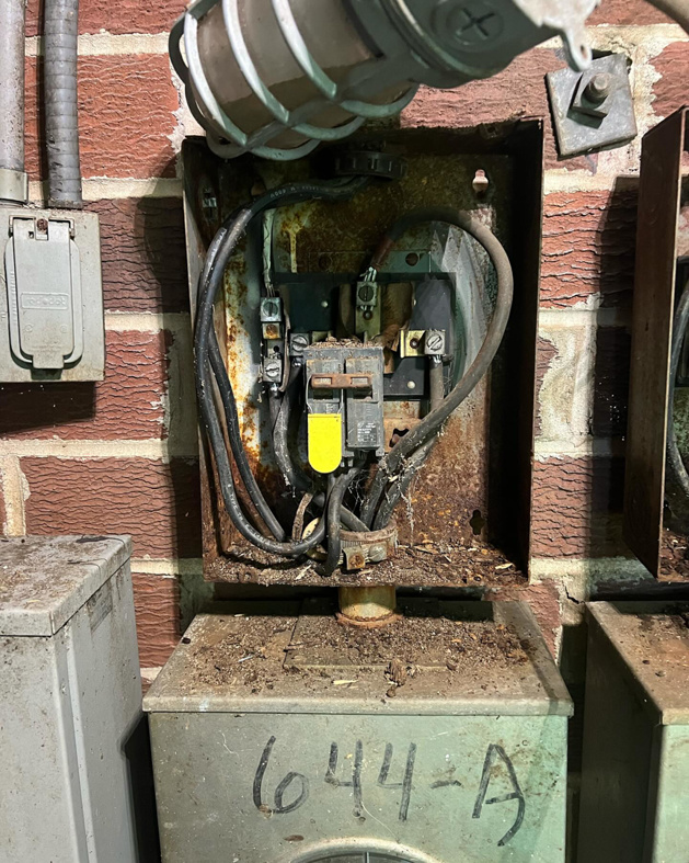An old electrical panel with a yellow-handled circuit breaker, showing signs of rust, serviced by Sapphire Electric LLC in Jonesboro, GA.