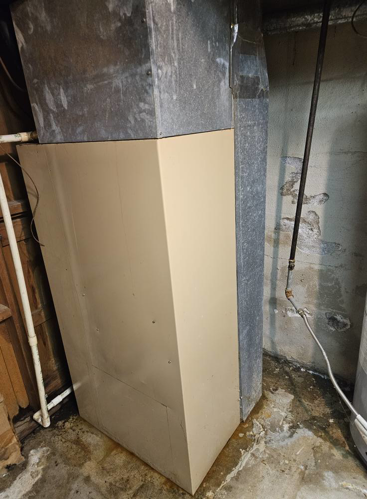 An older furnace or air handler unit in a basement, indicating potential HVAC service by Astron Services LLC in Wichita, KS.