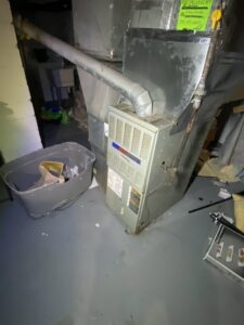 Old furnace and ductwork in a basement undergoing inspection by Breyer's Heating & Air Conditioning in Belleville, MI