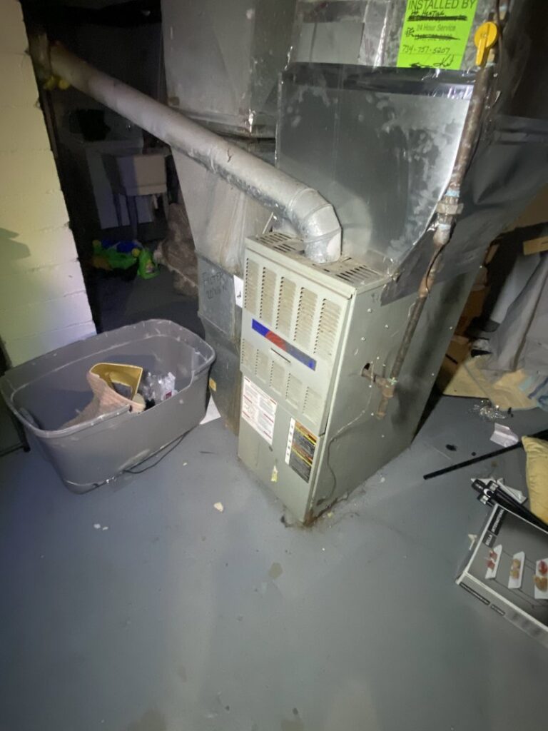 Old furnace and ductwork in a basement undergoing inspection by Breyer's Heating & Air Conditioning in Belleville, MI