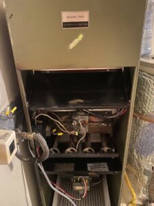 An old furnace with its panel open, showing burners and filter, likely undergoing inspection or repair by Number 1 Plumber in Washington, DC.