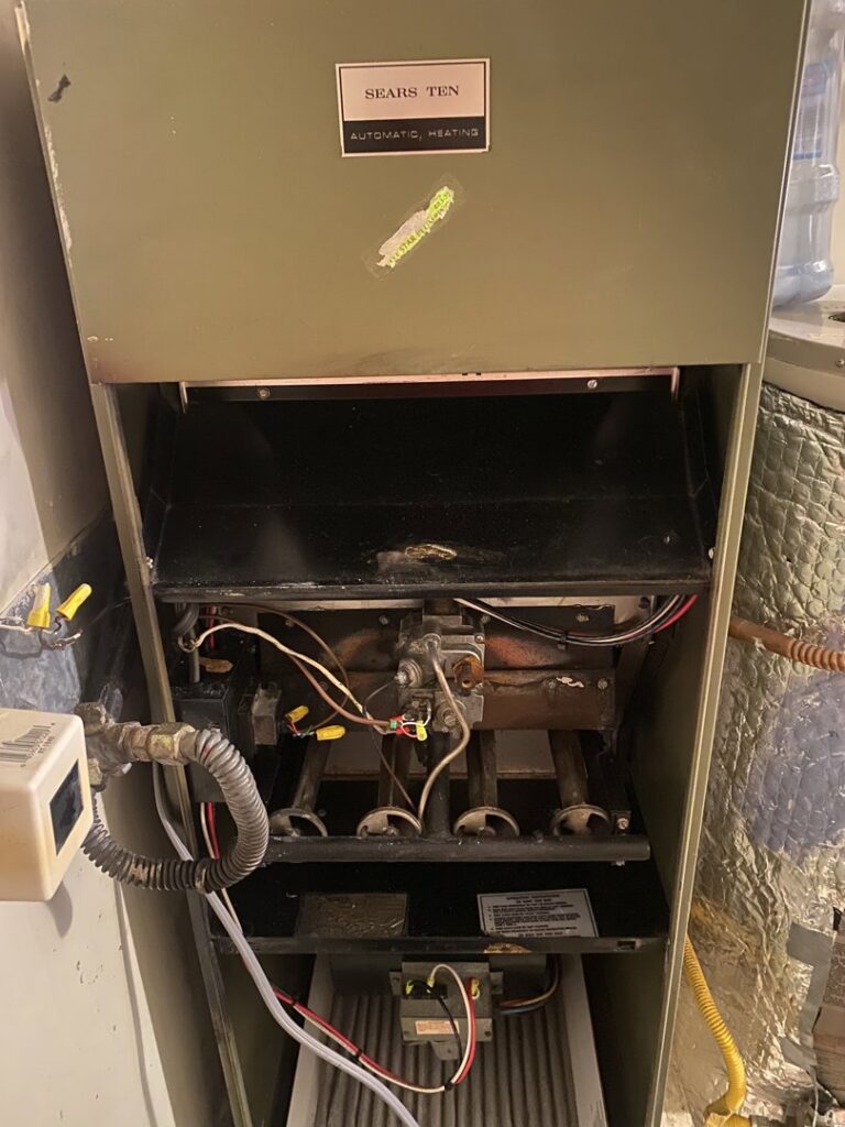 An old furnace with its panel open, showing burners and filter, likely undergoing inspection or repair by Number 1 Plumber in Washington, DC.