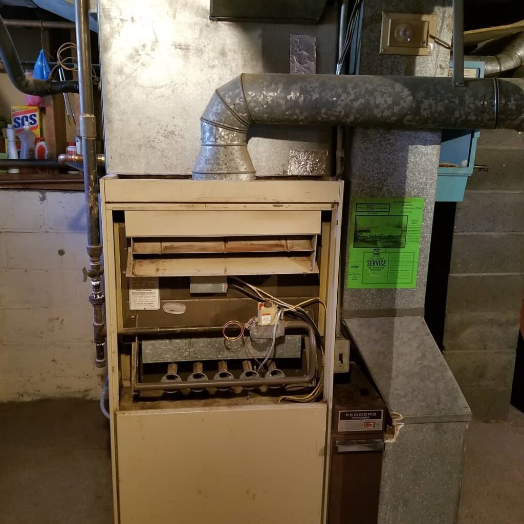 An older furnace with its front panel removed, showing internal components during repair by Batista Heating & Cooling, LLC. in Charlotte, NC.