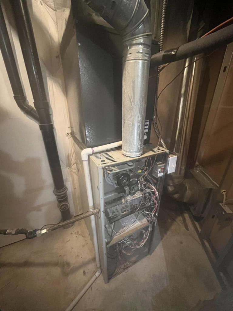 An old furnace with its panel removed, showing internal components during a repair or service by Nexus Heating & Air in Denver, CO.