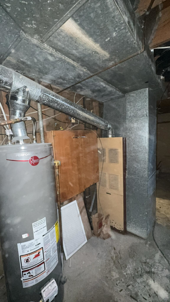 An older furnace and water heater system in a basement, ready for service or replacement by Nexus Heating & Air in Denver, CO.
