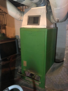 An old green furnace system in a basement, likely before replacement or during inspection by Allegheny General Contracting Services Heating and Cooling in Pittsburgh, PA.