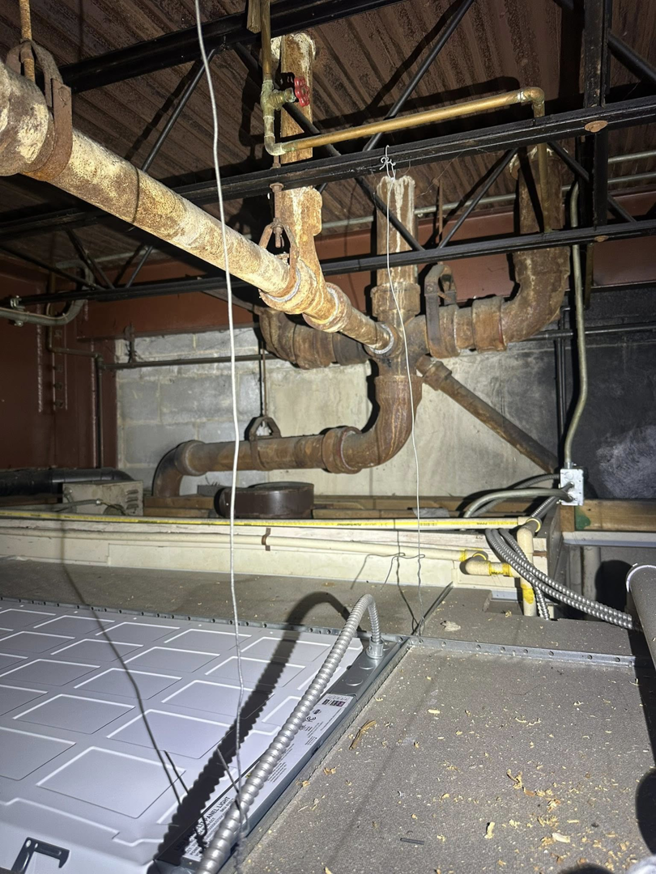 An inspection of old HVAC ductwork and rusty pipes in a utility area by Dynamic Comfort Solutions in York, PA.