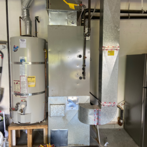 An older HVAC furnace and water heater system with ductwork, ready for service by Arctic Heating And Cooling in Chesapeake, VA.
