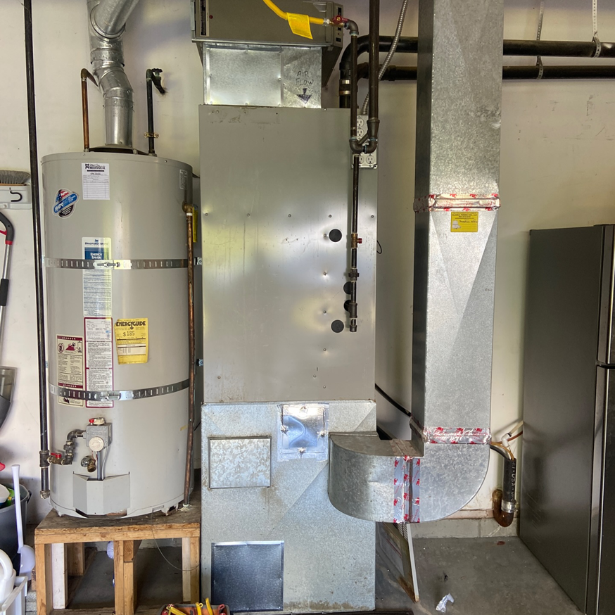 An older HVAC furnace and water heater system with ductwork, ready for service by Arctic Heating And Cooling in Chesapeake, VA.