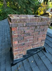An old, mossy brick chimney on a roof, indicating the need for repair by Five Star Chimney Repair in Hillsboro, OR.