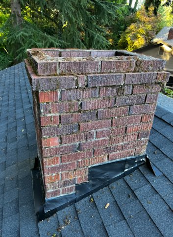 An old, mossy brick chimney on a roof, indicating the need for repair by Five Star Chimney Repair in Hillsboro, OR.