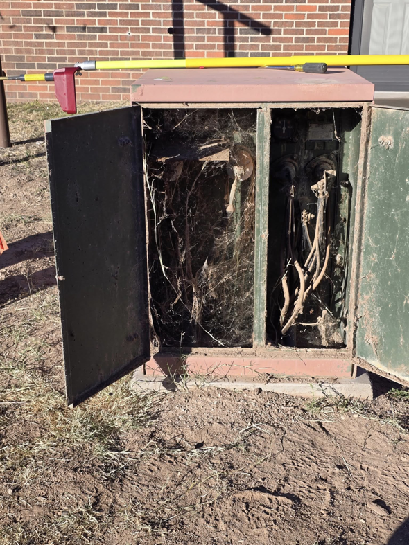 An old, cobweb-filled outdoor electrical box with open doors, indicating a need for repair or maintenance by Desert Wind Electric in Albuquerque, NM