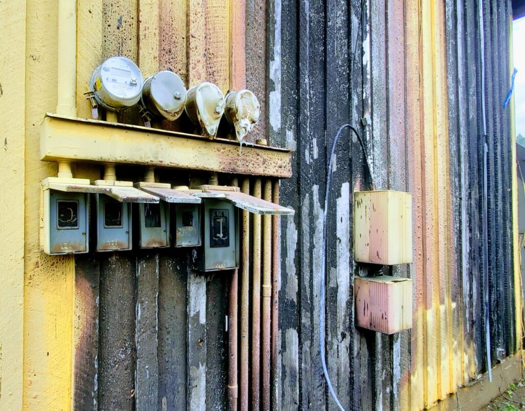Old outdoor electrical meters and service boxes on a weathered building, ready for service by Vets Electric Company in Tacoma, WA