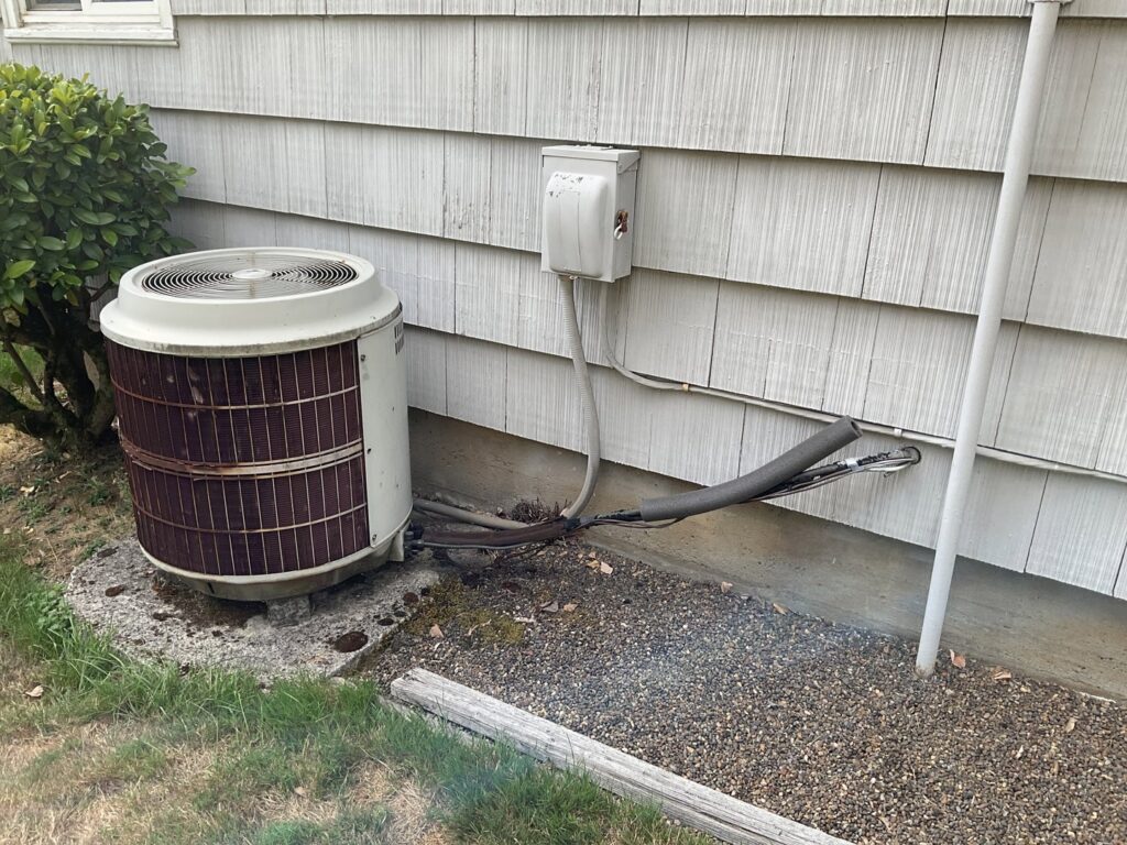 An older outdoor HVAC unit next to a residential building, ready for service or replacement by Gresham Heating and Air Conditioning in Wood Village, OR.