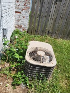 An old, overgrown outdoor air conditioning unit in need of service or replacement by Warren Mechanical, LLC in Carmel, IN.