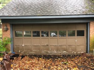 An old, peeling brown garage door with multiple windows, showing a before-replacement scenario by Door-Tech LLC in Lexington, KY.