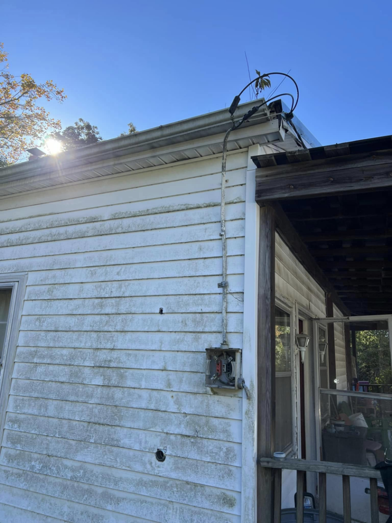 Old residential electrical service entry with exposed wiring and conduit on the side of a house, showing potential work for RJ Boyd Electric in Christiansburg, VA.