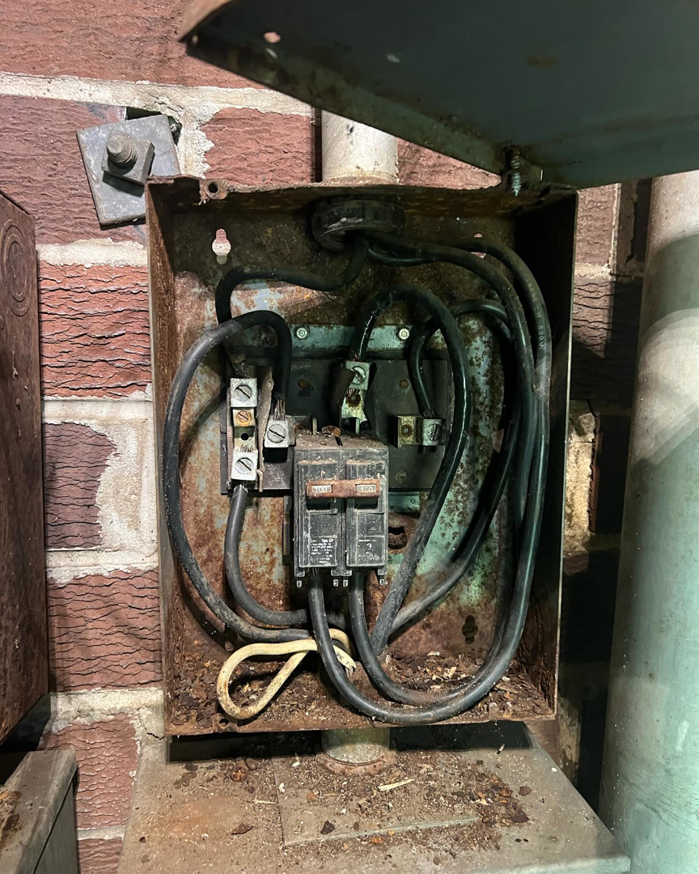 An old, rusty electrical panel with exposed wiring and circuit breakers, serviced by Sapphire Electric LLC in Jonesboro, GA.