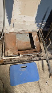 An old, rusty HVAC drain pan on the floor, indicating a need for replacement by Warren Mechanical, LLC in Carmel, IN.