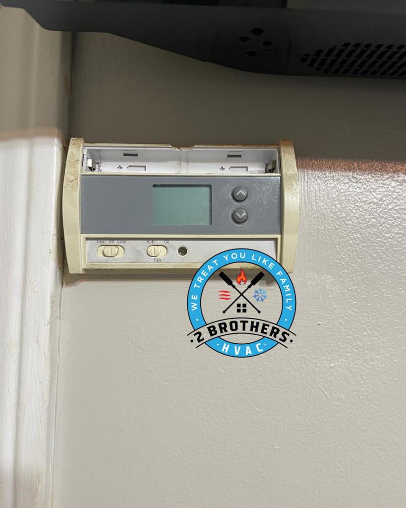 An old thermostat with its cover removed, showing internal wiring during an inspection by 2 Brothers HVAC in Seguin, TX